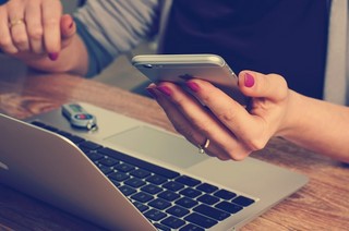 woman holding phone at computer